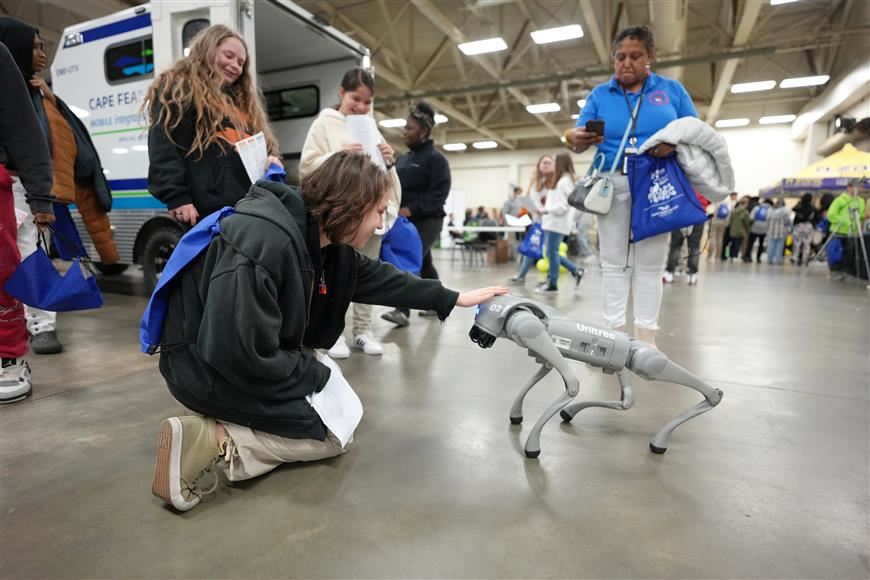 Student petting a robotic dog at the career fair while others observe.