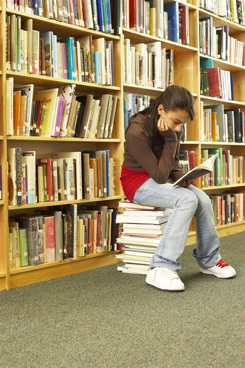 Image of a Female Student Reading a Book in Front of Library Shelves