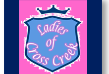 Image of a blue shield on a pink background with Ladies of Cross Creek in written in white with a pink glow inside the shield